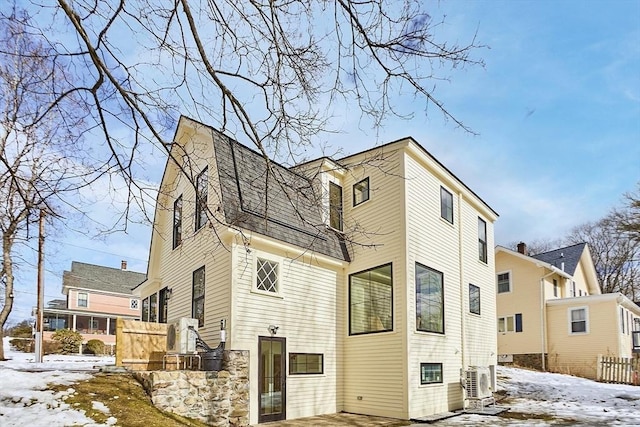 snow covered property featuring a shingled roof and a gambrel roof