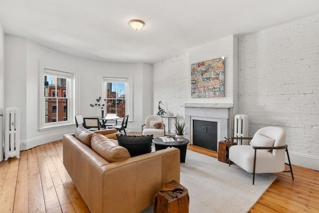 living room featuring baseboards, brick wall, light wood-style flooring, radiator heating unit, and a fireplace