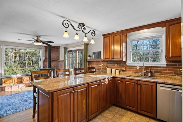 kitchen featuring a wood stove, sink, stainless steel dishwasher, decorative light fixtures, and kitchen peninsula