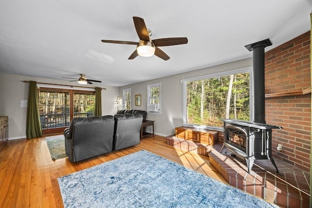 living room featuring wood-type flooring, a wood stove, and ceiling fan