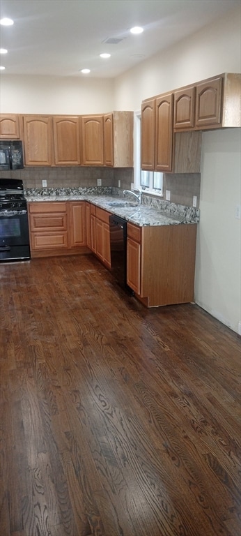 kitchen featuring light stone counters, black appliances, dark wood-type flooring, and backsplash