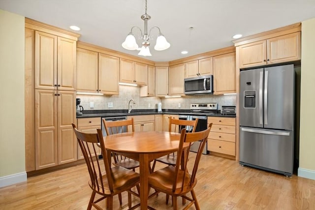 kitchen with light brown cabinets, light wood-type flooring, appliances with stainless steel finishes, dark countertops, and tasteful backsplash