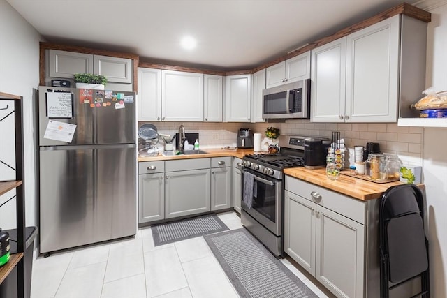 kitchen with butcher block counters, sink, tasteful backsplash, light tile patterned floors, and appliances with stainless steel finishes