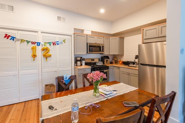 kitchen with tasteful backsplash, appliances with stainless steel finishes, gray cabinets, and light hardwood / wood-style floors