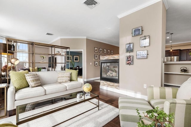 living room with crown molding, visible vents, dark wood-type flooring, and a glass covered fireplace