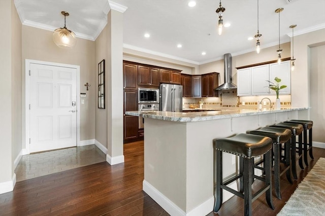 kitchen featuring stainless steel appliances, hanging light fixtures, wall chimney range hood, and a peninsula