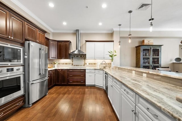 kitchen with appliances with stainless steel finishes, decorative light fixtures, wall chimney range hood, white cabinetry, and a sink