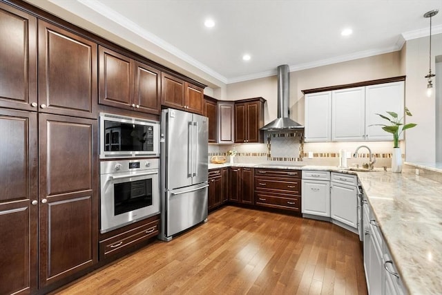 kitchen featuring a sink, appliances with stainless steel finishes, wall chimney range hood, decorative light fixtures, and crown molding