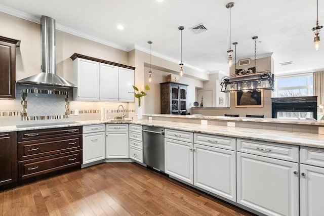 kitchen with hanging light fixtures, white cabinets, dishwasher, and wall chimney range hood