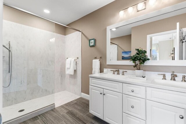 bathroom featuring double vanity, wood finished floors, walk in shower, and a sink