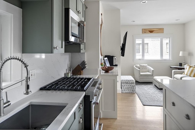 414 Sumner St Unit 1, Boston, MA 02128 - kitchen featuring stainless steel appliances, a sink, tasteful backsplash, light wood-style flooring, and light stone counters