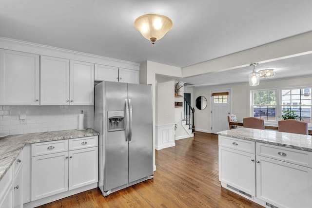 kitchen with white cabinets, stainless steel refrigerator with ice dispenser, light hardwood / wood-style flooring, backsplash, and light stone countertops