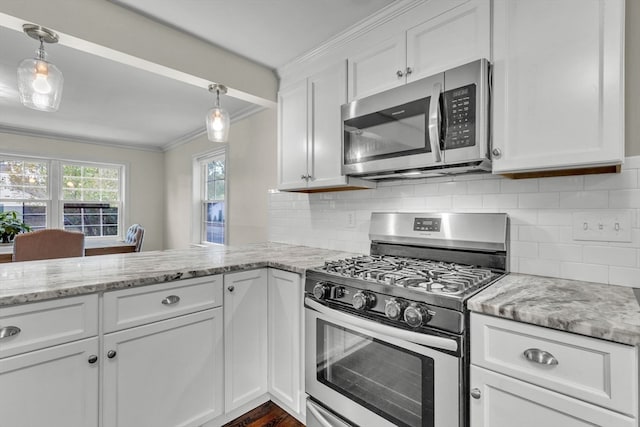 kitchen with appliances with stainless steel finishes, hanging light fixtures, white cabinets, light stone countertops, and crown molding