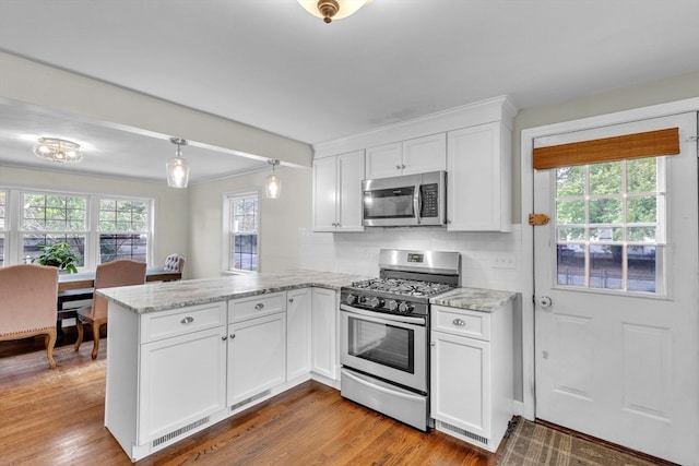 kitchen featuring appliances with stainless steel finishes, kitchen peninsula, hardwood / wood-style floors, and white cabinets