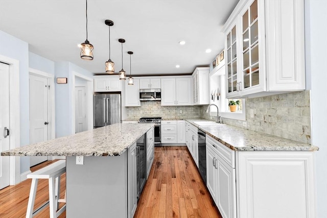 kitchen featuring light wood-style floors, a center island, white cabinets, a sink, and appliances with stainless steel finishes