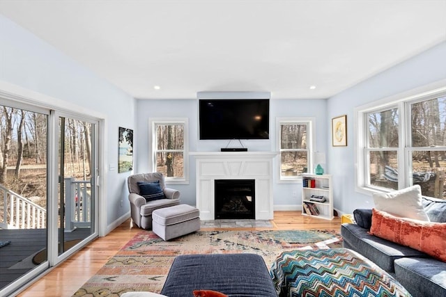 living area with light wood-type flooring, a fireplace with flush hearth, baseboards, and recessed lighting