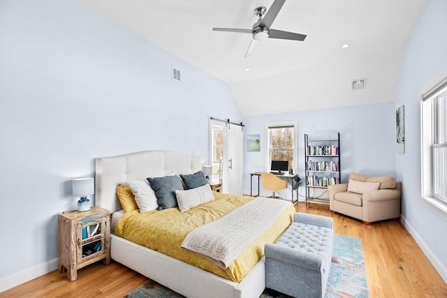bedroom with visible vents, a barn door, vaulted ceiling, and light wood-type flooring