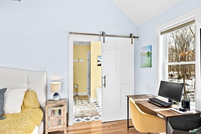 bedroom with vaulted ceiling, a barn door, and wood finished floors