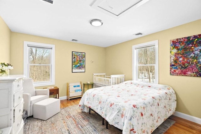 bedroom with visible vents, baseboards, wood finished floors, and multiple windows