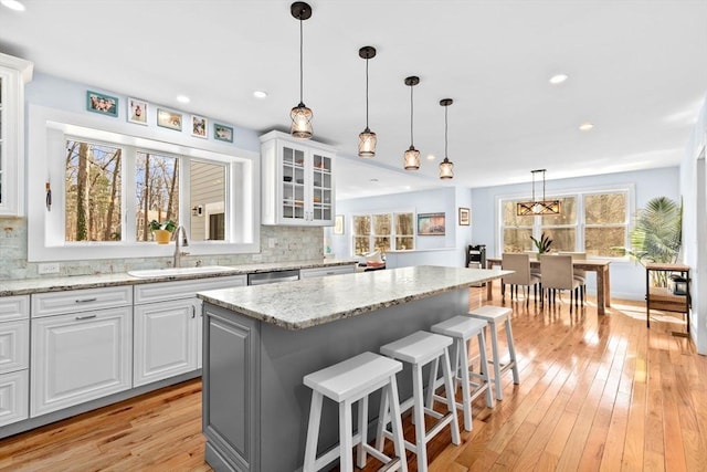 kitchen with glass insert cabinets, a sink, light wood finished floors, and tasteful backsplash