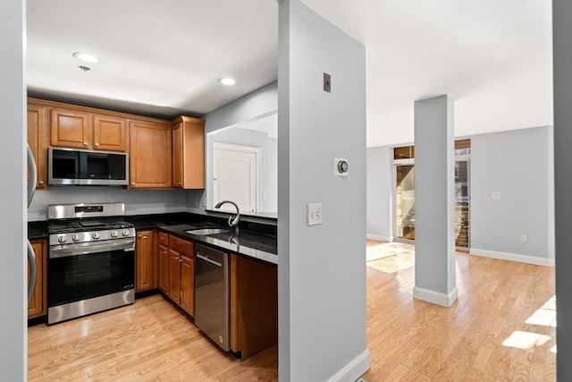 kitchen with stainless steel appliances, sink, light hardwood / wood-style flooring, and dark stone countertops