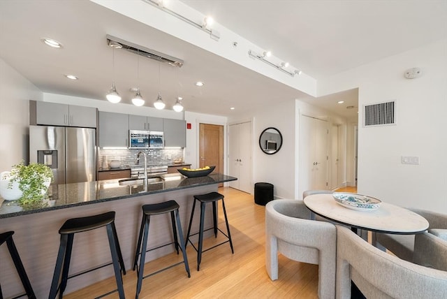 45 Province St Unit 1103, Boston, MA 02108 - kitchen featuring stainless steel appliances, a kitchen bar, backsplash, gray cabinetry, and light wood-style floors