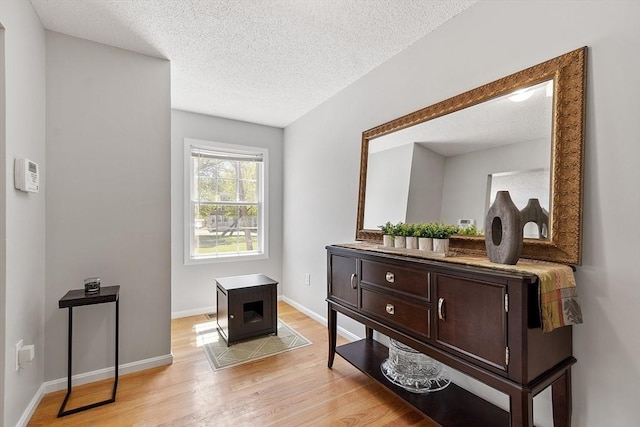 hall with light wood-type flooring, a textured ceiling, and baseboards