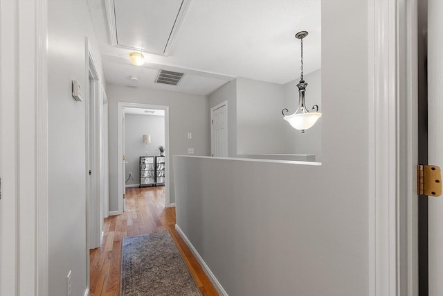 hall with light wood-style flooring, attic access, an upstairs landing, and baseboards