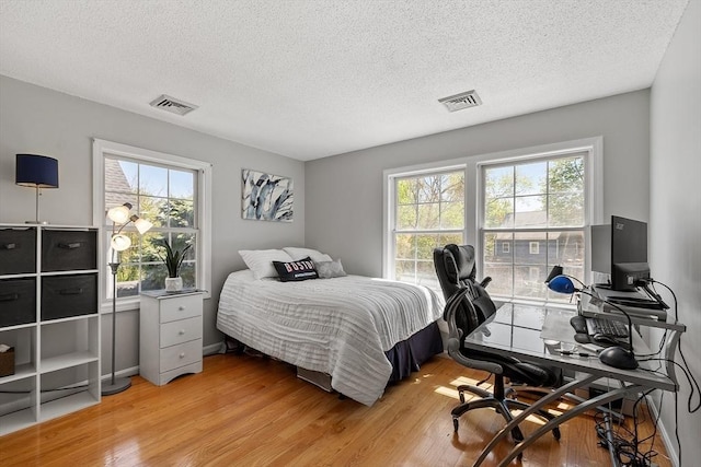 bedroom with light wood-type flooring, a textured ceiling, multiple windows, and a desk