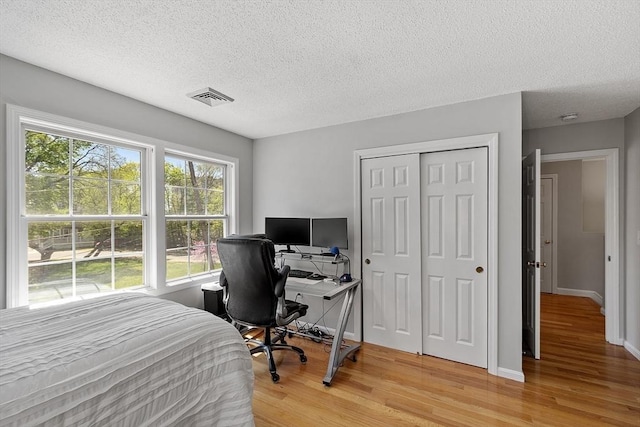 bedroom featuring light wood-style floors, a textured ceiling, a closet, baseboards, and a desk