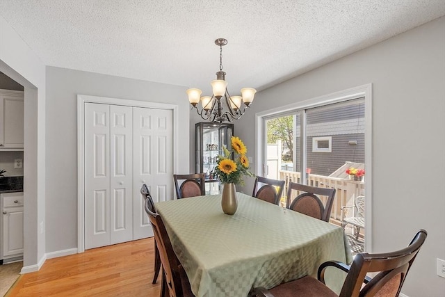 dining room with light wood finished floors, a chandelier, baseboards, and a textured ceiling