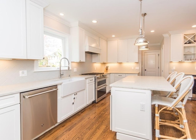 kitchen featuring stainless steel appliances, a sink, crown molding, a kitchen bar, and white cabinets