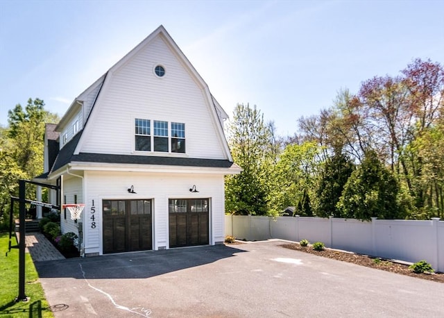 view of home's exterior featuring fence, a gambrel roof, an attached garage, and asphalt driveway