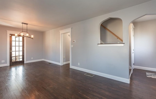 spare room featuring dark wood finished floors, baseboards, visible vents, and arched walkways