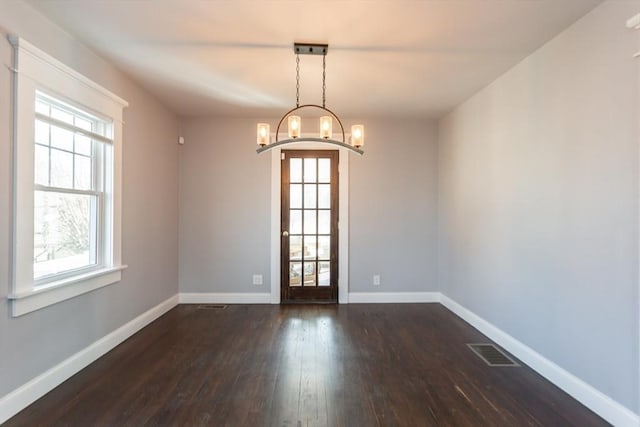 empty room with visible vents, an inviting chandelier, dark wood-type flooring, and baseboards