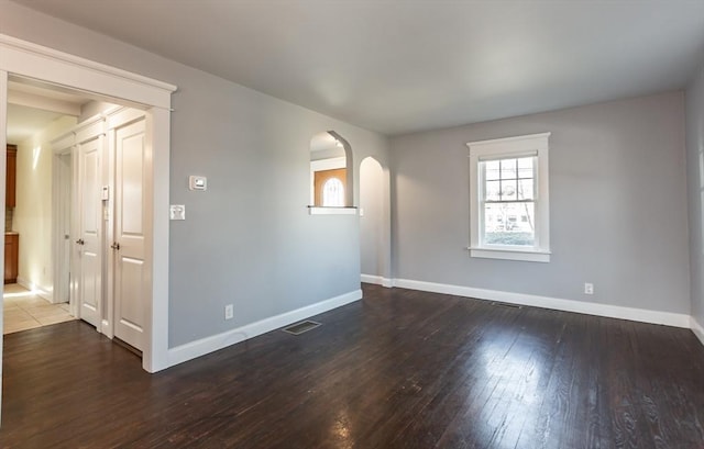 spare room with arched walkways, visible vents, baseboards, and wood finished floors