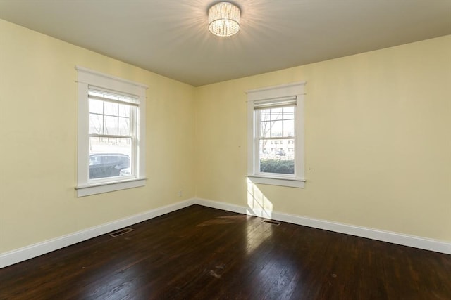 unfurnished room featuring visible vents, plenty of natural light, baseboards, and dark wood-style flooring