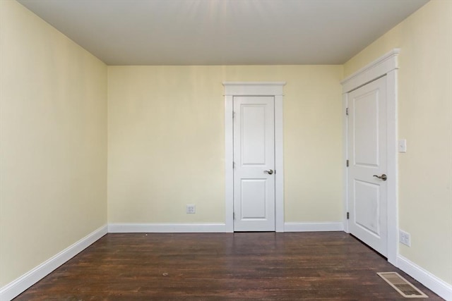 empty room featuring dark wood-type flooring, baseboards, and visible vents