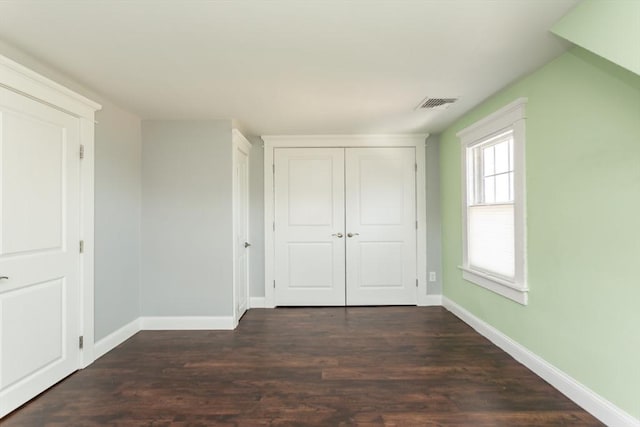 unfurnished bedroom with a closet, visible vents, dark wood-type flooring, and baseboards