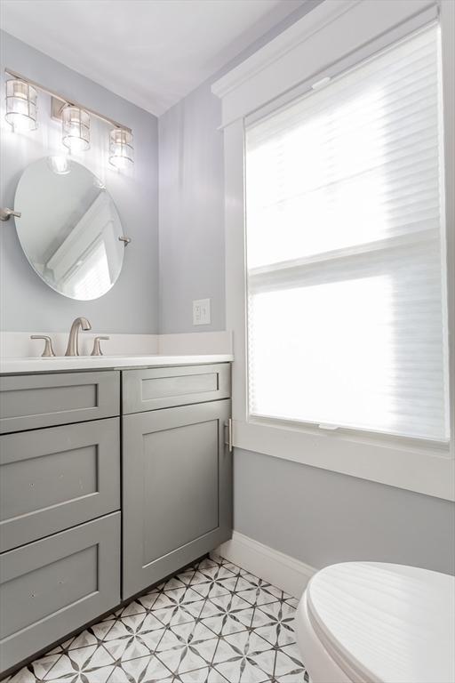 half bathroom featuring tile patterned floors, baseboards, toilet, and vanity