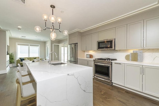 kitchen featuring sink, light stone counters, decorative light fixtures, a center island with sink, and appliances with stainless steel finishes