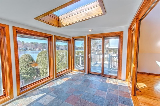 unfurnished sunroom featuring a skylight, baseboards, a water view, and stone finish flooring