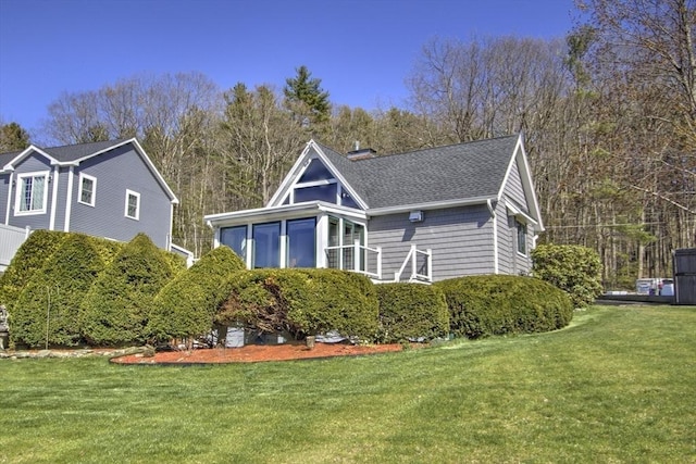 exterior space featuring a sunroom, a chimney, roof with shingles, and a front lawn