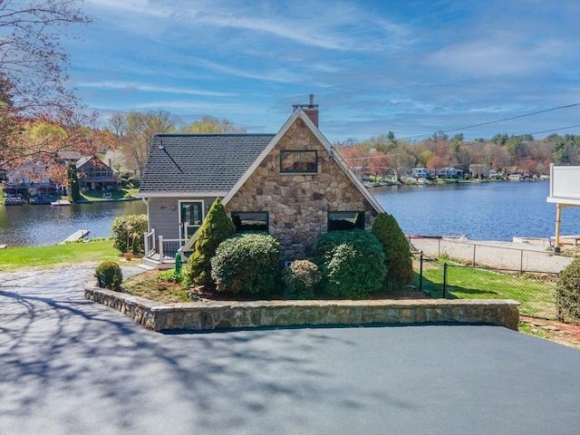 view of side of home featuring a water view, fence, a chimney, and stone siding