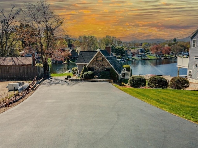 view of front of property with fence, a front lawn, stone siding, a water view, and a chimney