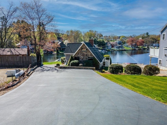 view of front of home featuring fence, stone siding, a front yard, a water view, and a chimney
