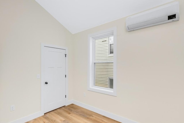 unfurnished room featuring lofted ceiling, baseboards, a wall mounted air conditioner, and light wood finished floors