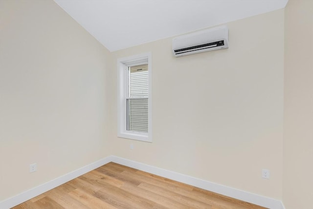 spare room featuring light wood-type flooring, an AC wall unit, vaulted ceiling, and baseboards