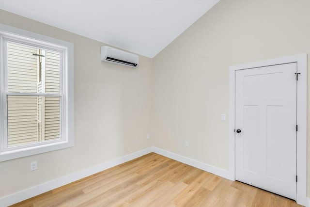 unfurnished room with a wall mounted air conditioner, vaulted ceiling, light wood-style flooring, and baseboards