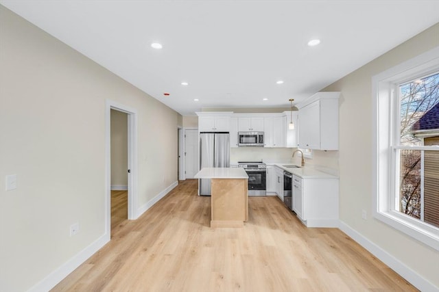 kitchen with white cabinets, a kitchen island, stainless steel appliances, light countertops, and a sink